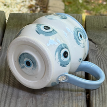 Load image into Gallery viewer, Ceramic mug with blue and black eye design on a wooden surface