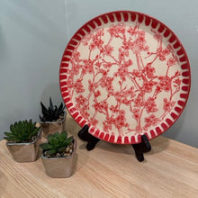 Load image into Gallery viewer, Decorative plate with red floral pattern on a stand, surrounded by small potted plants on a wooden surface.