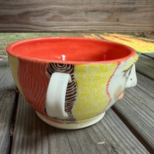Load image into Gallery viewer, Pottery bowl with orange interior and girl face on outside sitting on wood with trees in the background