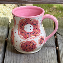 Load image into Gallery viewer, Decorative mug with pink interior, pink handle, and donut design sitting on a wooden surface.