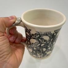 Load image into Gallery viewer, Hand holding a ceramic mug with black and white pattern on a plain background