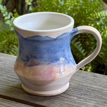Load image into Gallery viewer, Ceramic mug with blue and pink gradient on a wooden surface with greenery in the background
