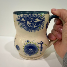 Load image into Gallery viewer, Ceramic mug with blue floral patterns held by a hand on a white background
