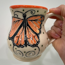 Load image into Gallery viewer, Ceramic mug with butterfly design held by a hand against a white background
