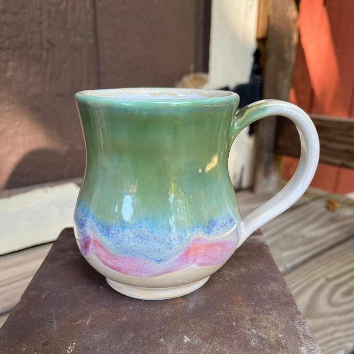 Green ceramic mug with multicolored base on a metal surface