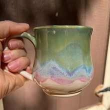 Load image into Gallery viewer, Hand holding a ceramic mug with a colorful design against a blurred background

