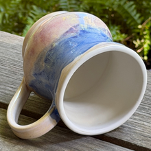 Load image into Gallery viewer, Ceramic mug with a multicolored design on a wooden surface with a green leafy background

