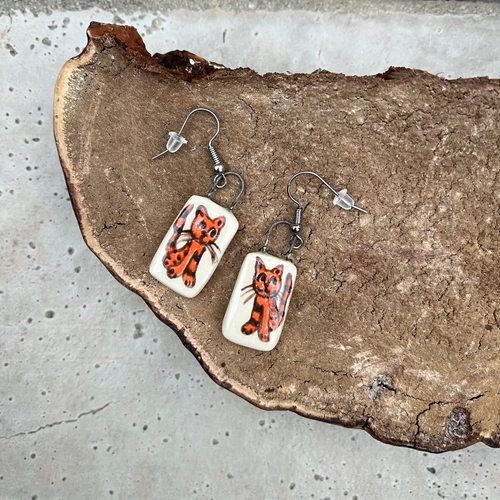 Pair of earrings with cat designs on a rustic stone and mushroom surface
