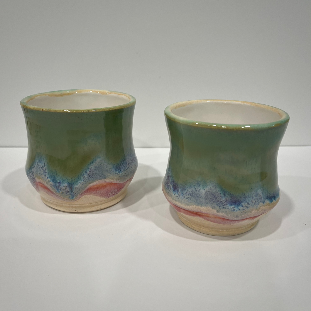 Two ceramic cups with green glaze and colorful base on a white background