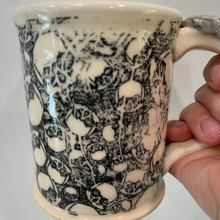 Load image into Gallery viewer, Mug with black and white pattern held by a hand against a plain background
