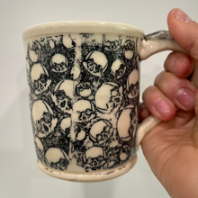 Load image into Gallery viewer, Mug with skull pattern held by a hand against a white background

