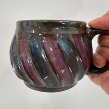 Load image into Gallery viewer, Hand holding a ceramic mug with ribbed texture and multicolored glaze against a plain background
